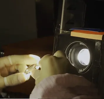 A close-up of an optical lens being inspected under a high-intensity light source to verify multi-layer coating quality and light transmission clarity in a controlled environment.