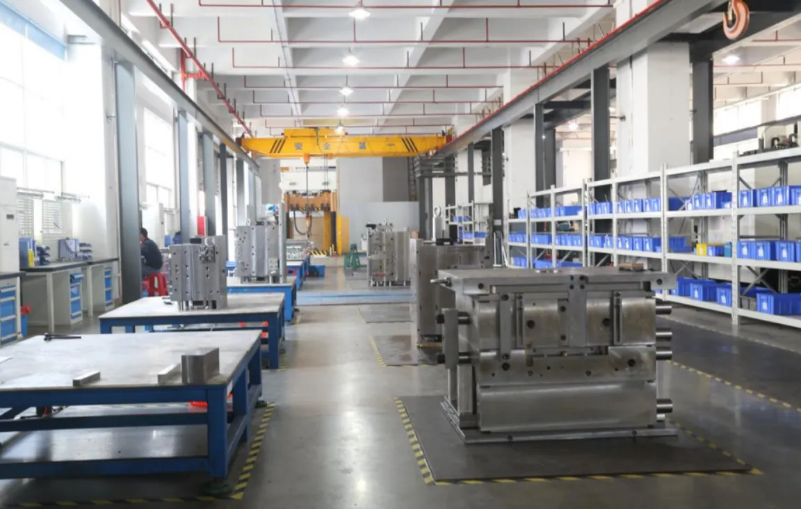 A spacious industrial workshop equipped with overhead cranes and heavy-duty workbenches, showing multiple precision steel molds in the assembly stage with organized component storage in the background