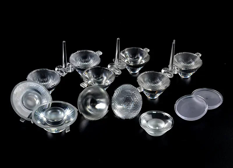 A collection of clear TIR lenses and aspheric components on a black background, featuring intricate honeycomb micro-textures and precisely molded internal reflection surfaces for beam shaping.