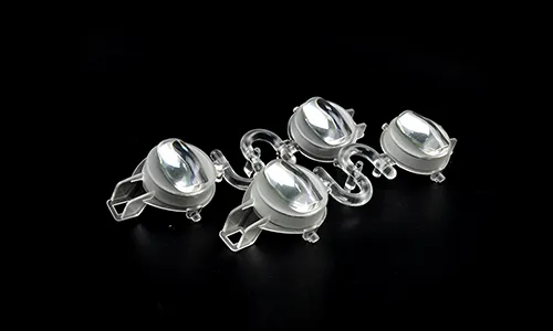 An injection-molded four-cavity clear optical lens array connected by a winding plastic runner system on a solid black background, with each lens unit featuring a raised longitudinal asymmetric curved surface and integrated mounting brackets.