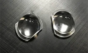 A 16-cavity transparent plastic injection-molded street light lens array component layout on a black brushed surface, showing a central vertical sprue branching out into a symmetrical runner system that connects 16 individual rectangular optical lens units.