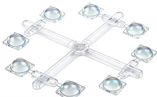 An injection-molded Fresnel lens array component with a cross-shaped clear plastic runner system, featuring eight circular sensing lens units with fine concentric microstructures on a white background.