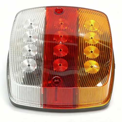 A tricolor square LED rear combination tail light lens for trucks and trailers, isolated on a white background. The PMMA/PC component is divided into three functional color zones: clear for reverse, red for stop/tail, and amber for turn signal. Each section features vertical light diffusion fluting and four integrated circular Fresnel optics for optimized optical performance, manufactured via multi-material injection molding.