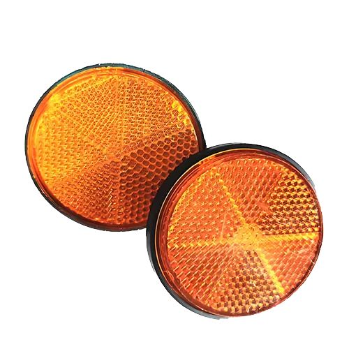 A pair of round amber (orange-yellow) safety reflex reflectors for trucks and motorcycles, isolated on a white background. The components feature black plastic housing rims and intricate internal micro-prismatic corner-cube optic arrays designed to return light back to its source, highlighting high-precision optical micro-structure injection molding.